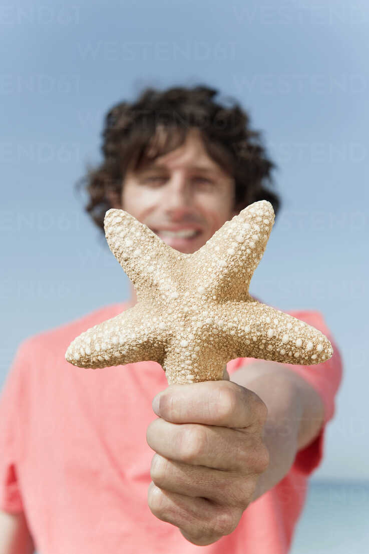 Spain, Mallorca, Young man holding starfish, smiling, portrait – Stockphoto