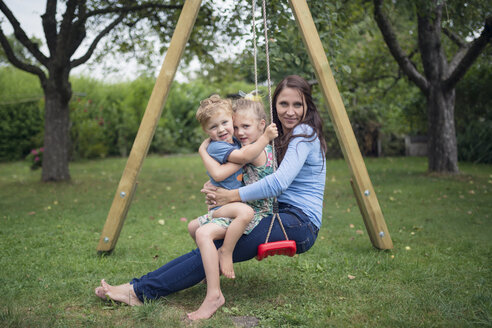 Mother Sitting With Her Two Little Children On A Swing In The Garden Stockphoto