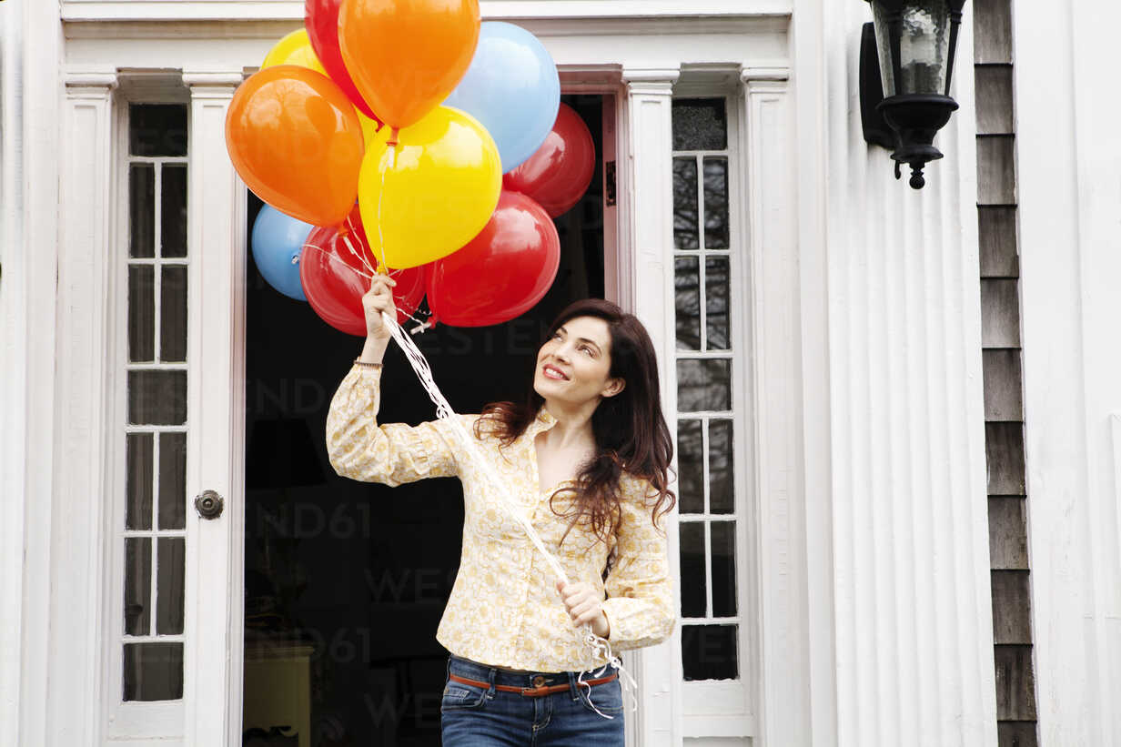 Woman Holding Helium Balloons While Standing Outside House Cavf Cavan Images Westend61