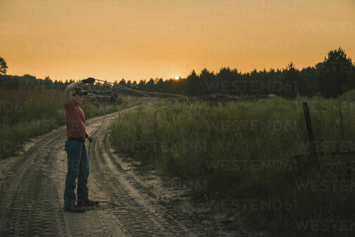 Full Length Of Boy Lassoing While Standing Against Clear Sky During Sunset Stockphoto