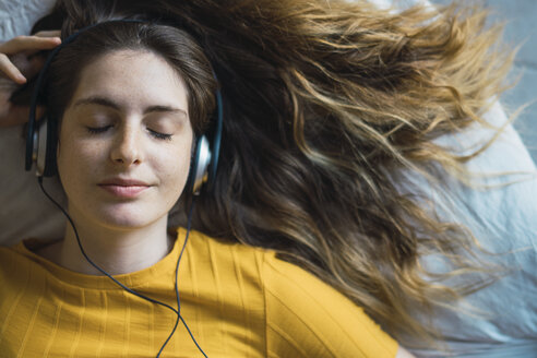 Young woman lying on bed listening music with headphones and smartphone - KKAF00976 - Kike Arnaiz/Westend61