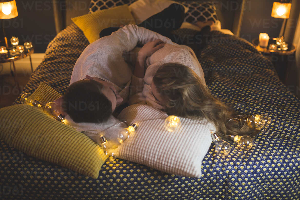 Romantic Young Couple Cuddling In Bed With Fairy Lights