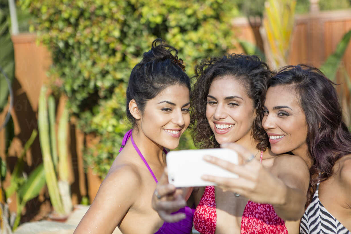 Three adult sisters wearing bikini tops posing for smartphone selfie in  garden - ISF13215 - Deborah Kolb/Westend61