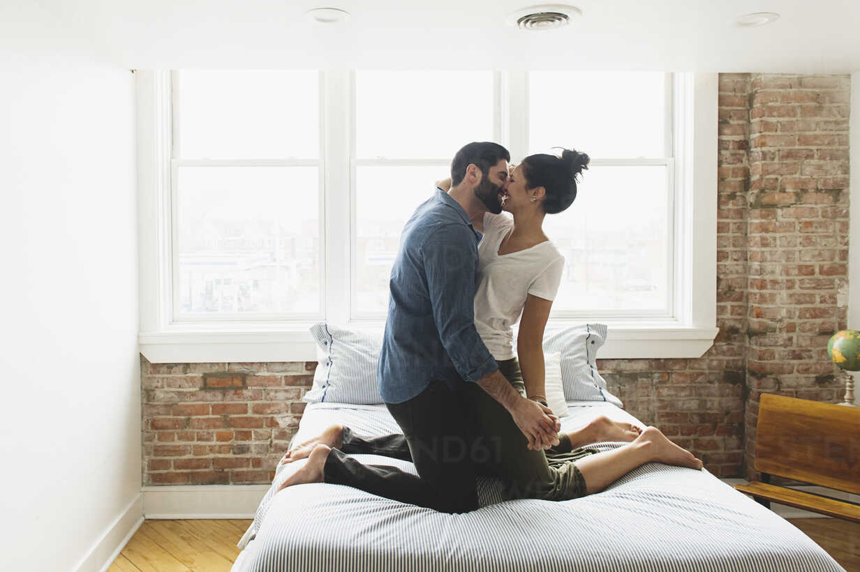 Romantic Couple Kissing While Kneeling On Bed At Home Stockphoto