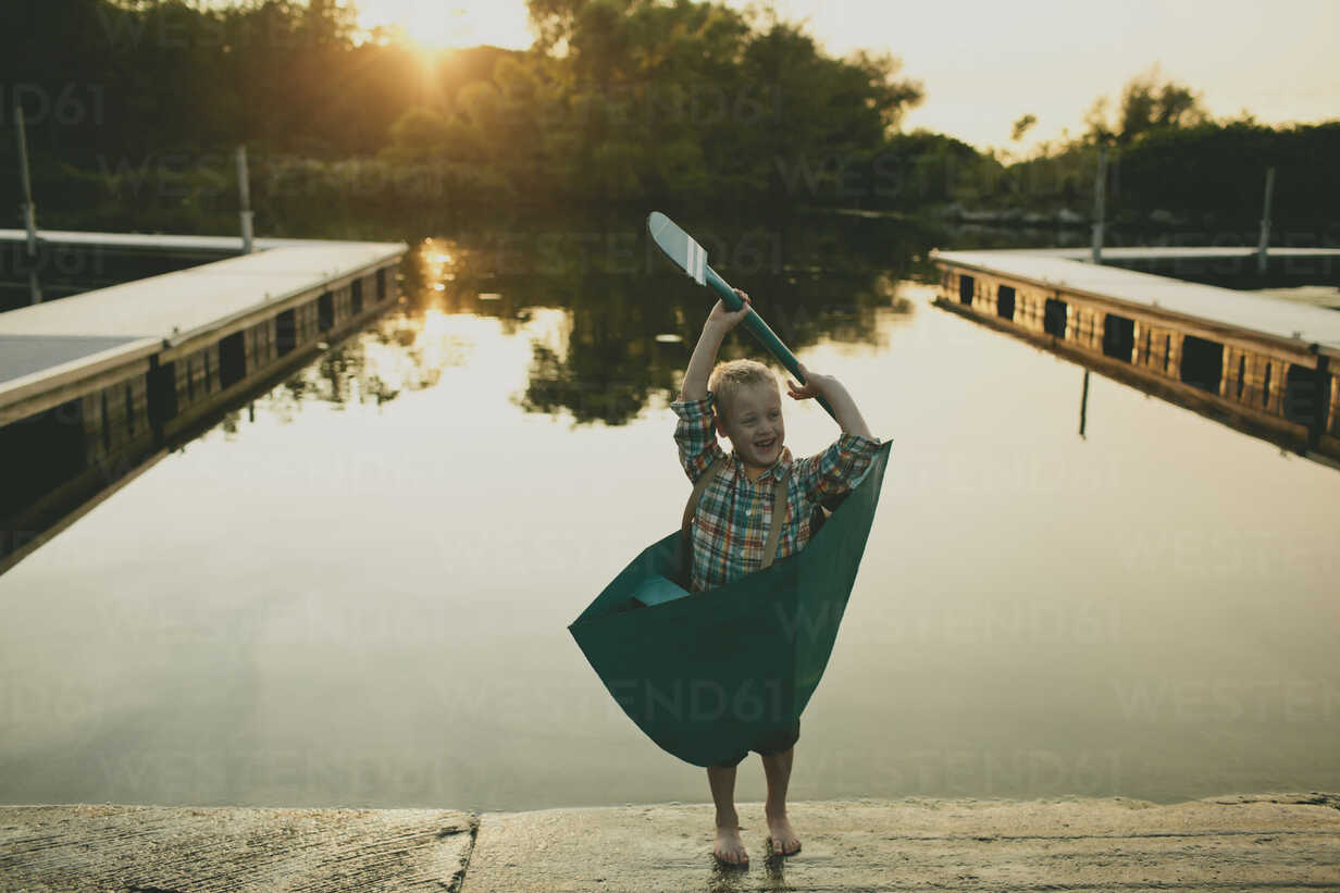 Happy Boy Wearing Boat Costume While Standing By Lake During Sunset Stockphoto