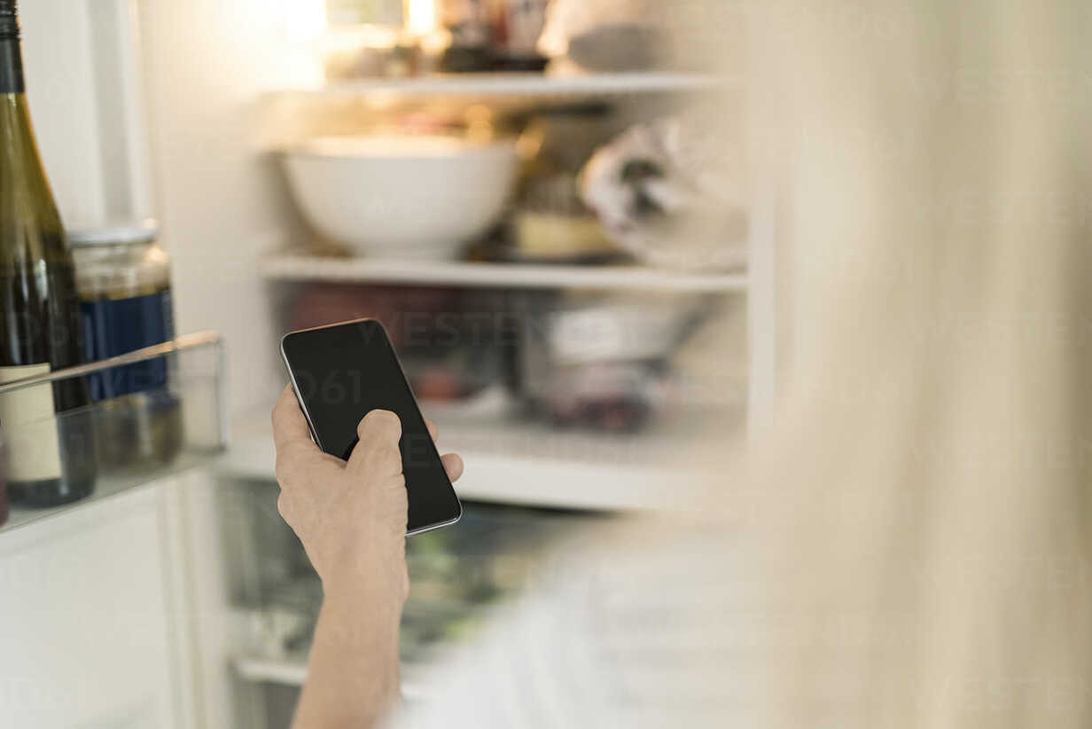 Hand Of Woman With Smartphone Checking Fridge In Kitchen At Smart Home Stockphoto