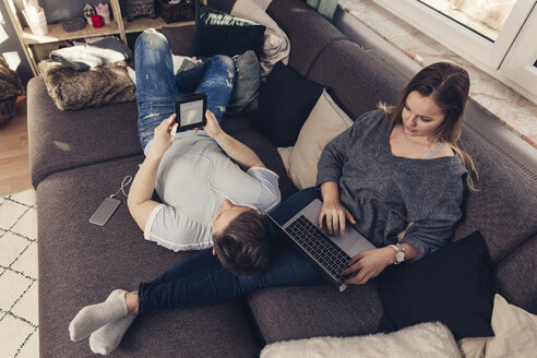 Young couple relaxing on sofa and using notebook, smartphone and ebook reader - SEBF00090 - Sebastian Dorn/Westend61