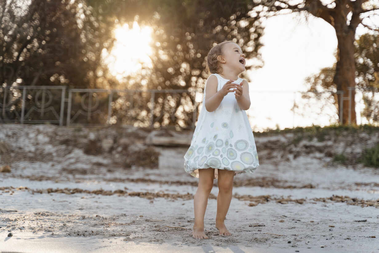 Laughing Cute Toddler Girl Standing On The Beach At Sunset Stockphoto