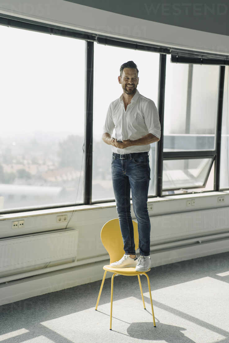 happy mature businessman standing on yellow chair in empty