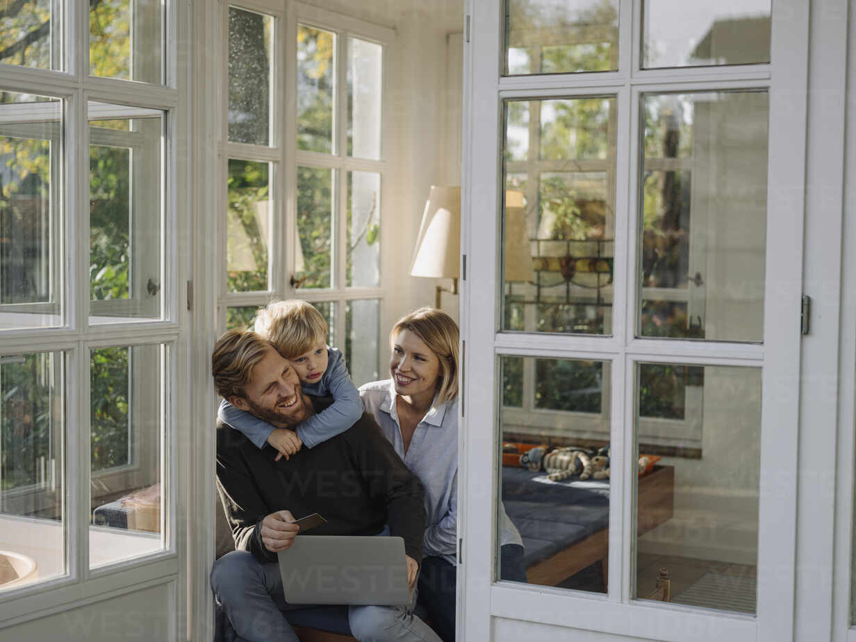 Family Using Laptop And Credit Card In Sunroom At Home Stockphoto