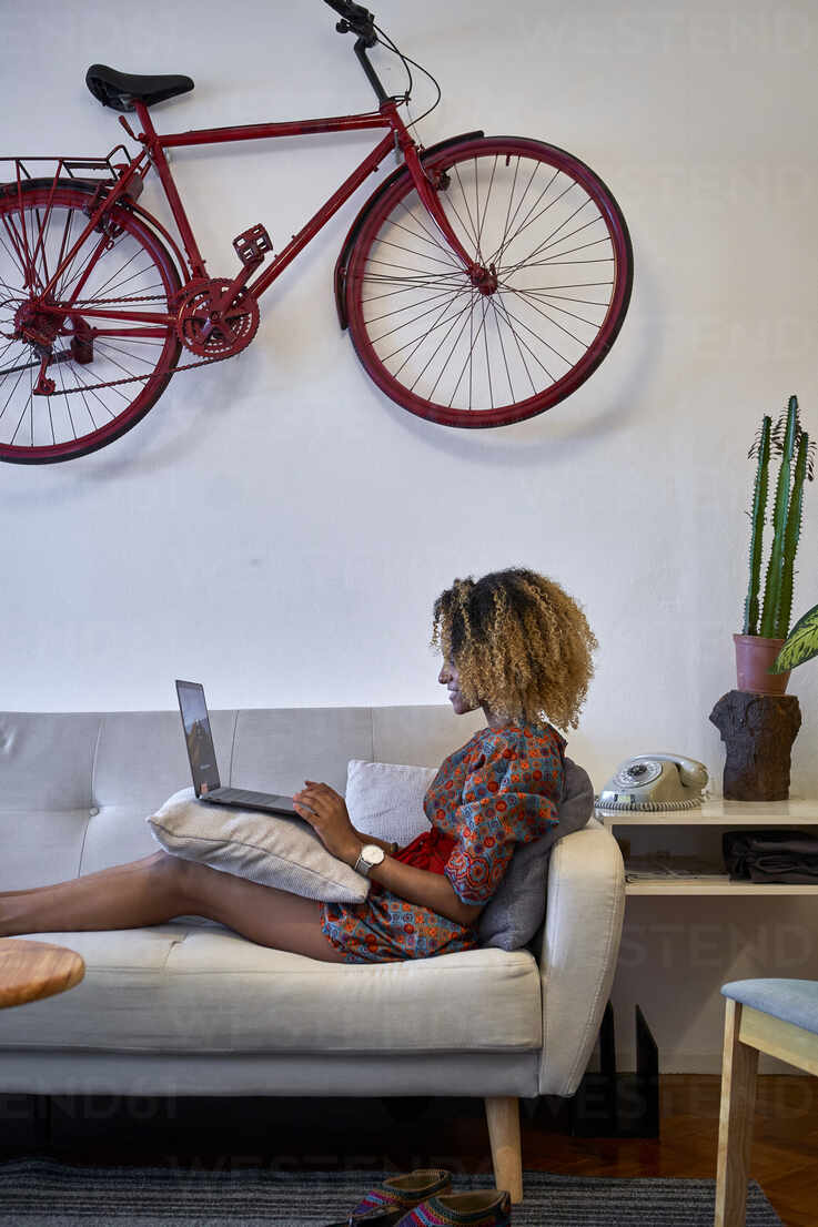 Woman Using Laptop In Living Room At Home With Vintage Bicycle Hanging On The Wall Stockphoto