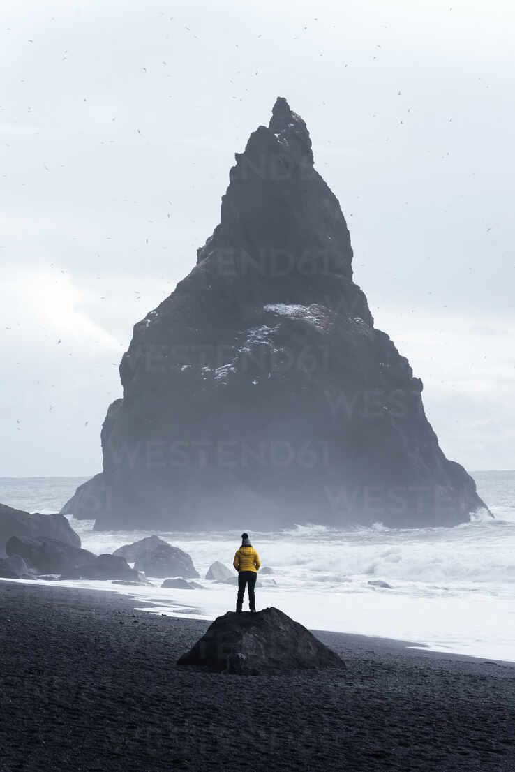 Distant Traveler Standing On Stone On Seashore And Admiring Stormy Sea Water And Huge Rough Stone