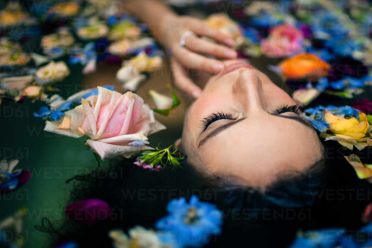 From Above Attractive Female Touching Face While Lying In Bathtub With Warm Water And Various Colorful