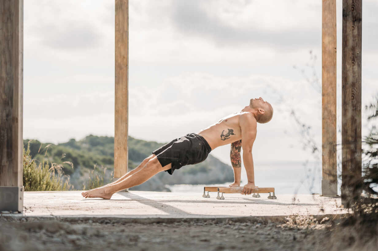 Side View Of Male Athlete With Muscular Torso Performing Handstand On Parallel Bars During Workout In